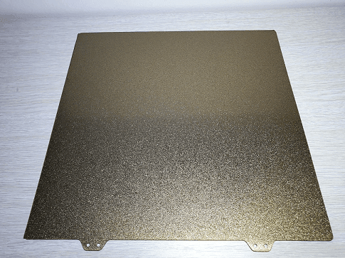 Textured Pei Build Plate 1 A flat, metallic sheet with a textured golden surface, featuring rounded corners and two holes at the bottom for mounting.