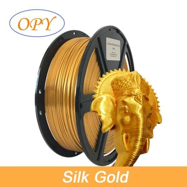 A spool of golden silk filament for 3D printing, with a decorative golden elephant figure partially visible in front.