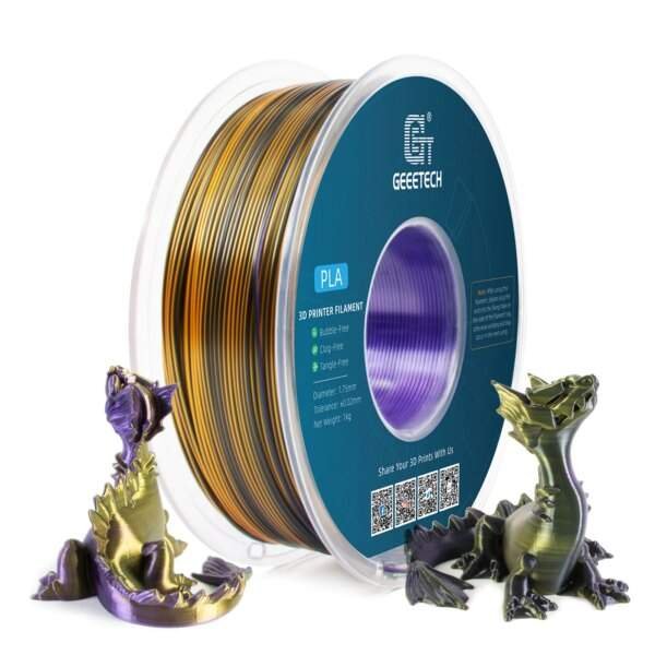A spool of 3D printer filament in gold and purple, with two dragon figures printed in the same colour scheme placed beside it.