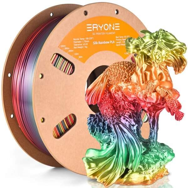 A spool of 3D printer filament, labelled "Silk Rainbow PLA," is shown with vibrant rainbow colours, beside a detailed, multicoloured 3D printed model of a fish. The spool has a cardboard base and a central opening displaying the filament.