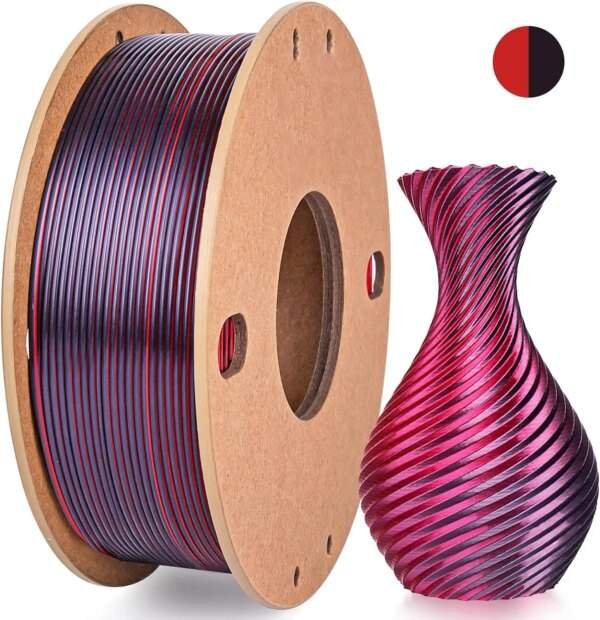 A spool of dual-coloured 3D printing filament in shades of purple and red, next to a decorative vase with a spiralled design, also in purple and red. A small colour swatch showing the filament colours is in the upper right corner.