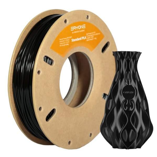 A spool of black 3D printer filament on a cardboard reel with an orange label, alongside a decorative black vase-like object made from the filament.