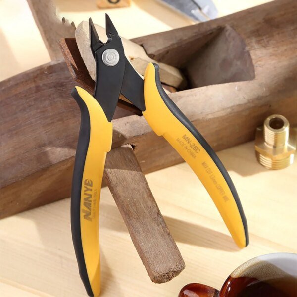 A pair of yellow and black cutting pliers placed on a wooden surface, with a piece of wood partially held by the pliers and various tools in the background.